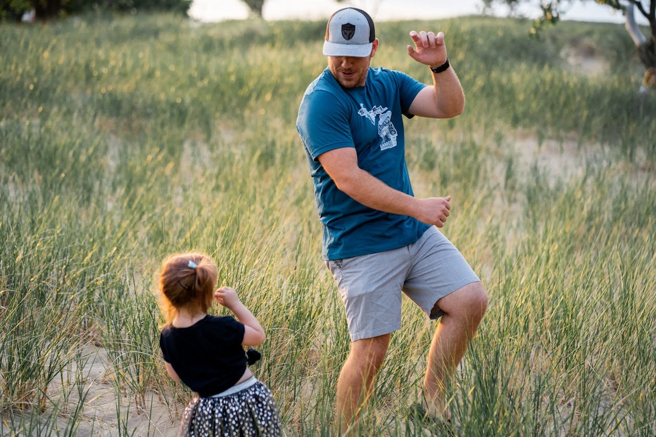 A father dances playfully with his daughter in a sunny field, capturing joy and bonding.