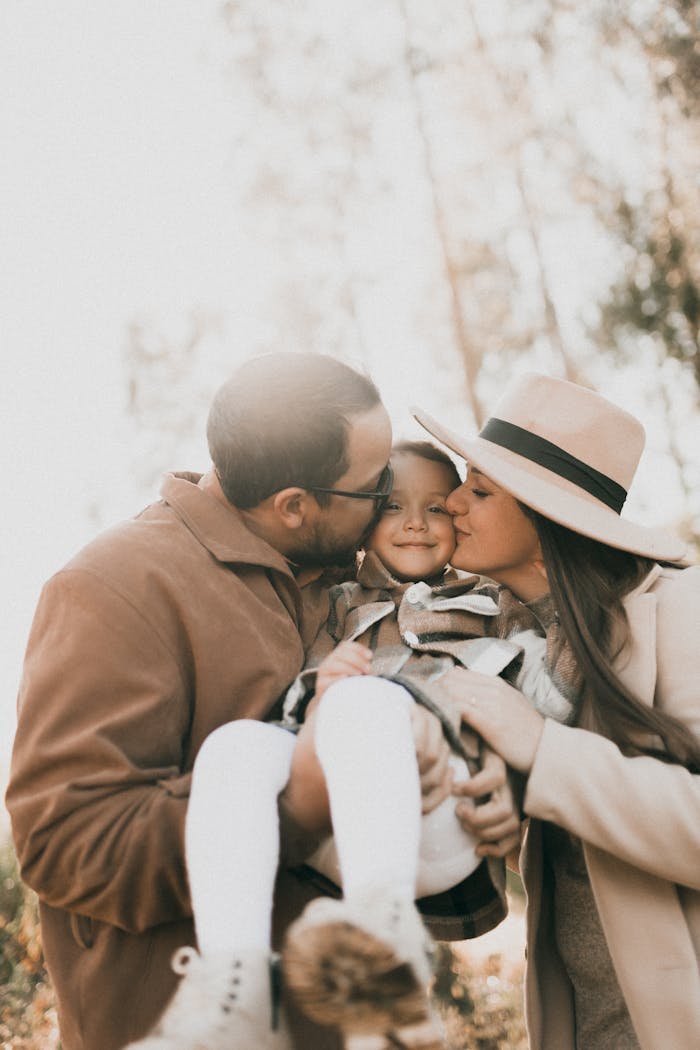 A heartwarming moment of parents hugging and kissing their young child outdoors in a sunlit setting.