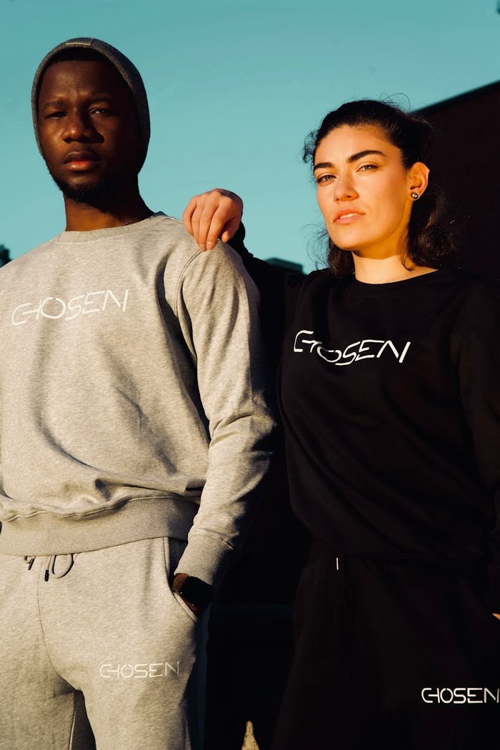 A couple poses in stylish Chosen sweatshirts under bright outdoor daylight.